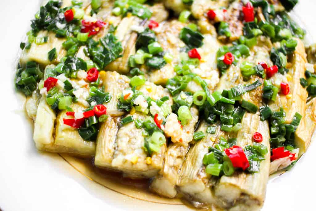 small bowl with grilled eggplant, scallions and chilis in front of a plate of eggplant