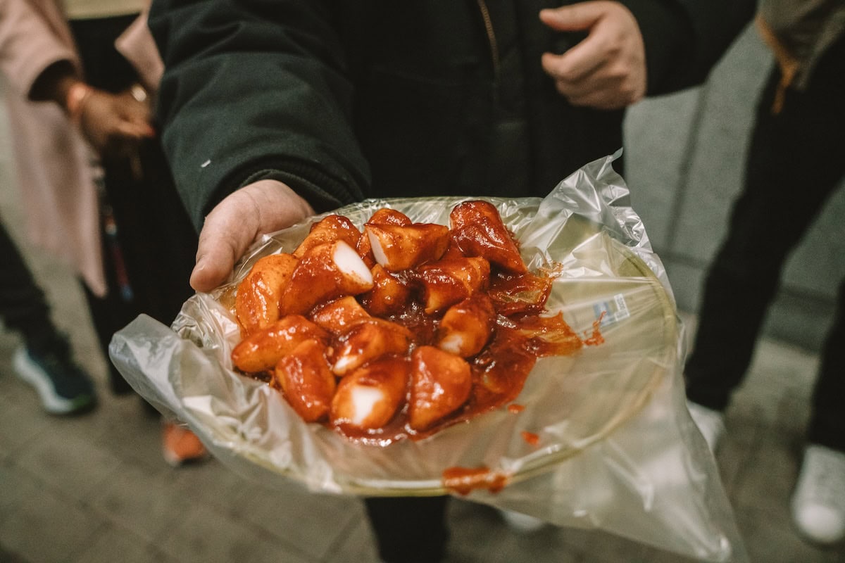 Man holds out a plate of tteokbokki