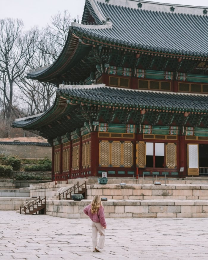 Michelle stands looking out at a traditional Korean palace with stone steps and ornate detailing in the architecture