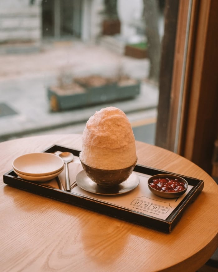 Piled high shaved ice in a dish on a wooden table.