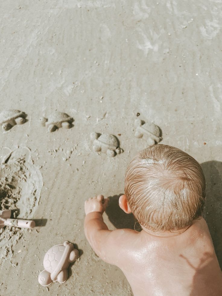 Bé ngồi vẽ hình trên cát với que gỗ nhỏ