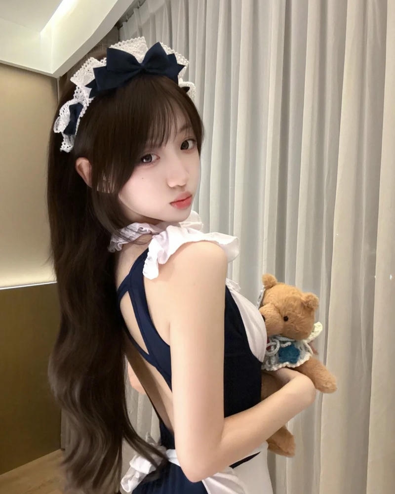 Cosplay hầu gái tóc nâu ôm gấu bông đứng bên rèm