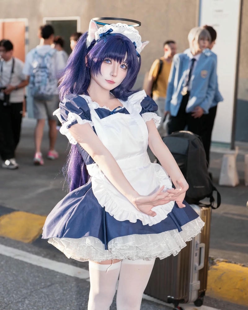 Maid tóc tím váy xanh đứng giữa phố đông người qua