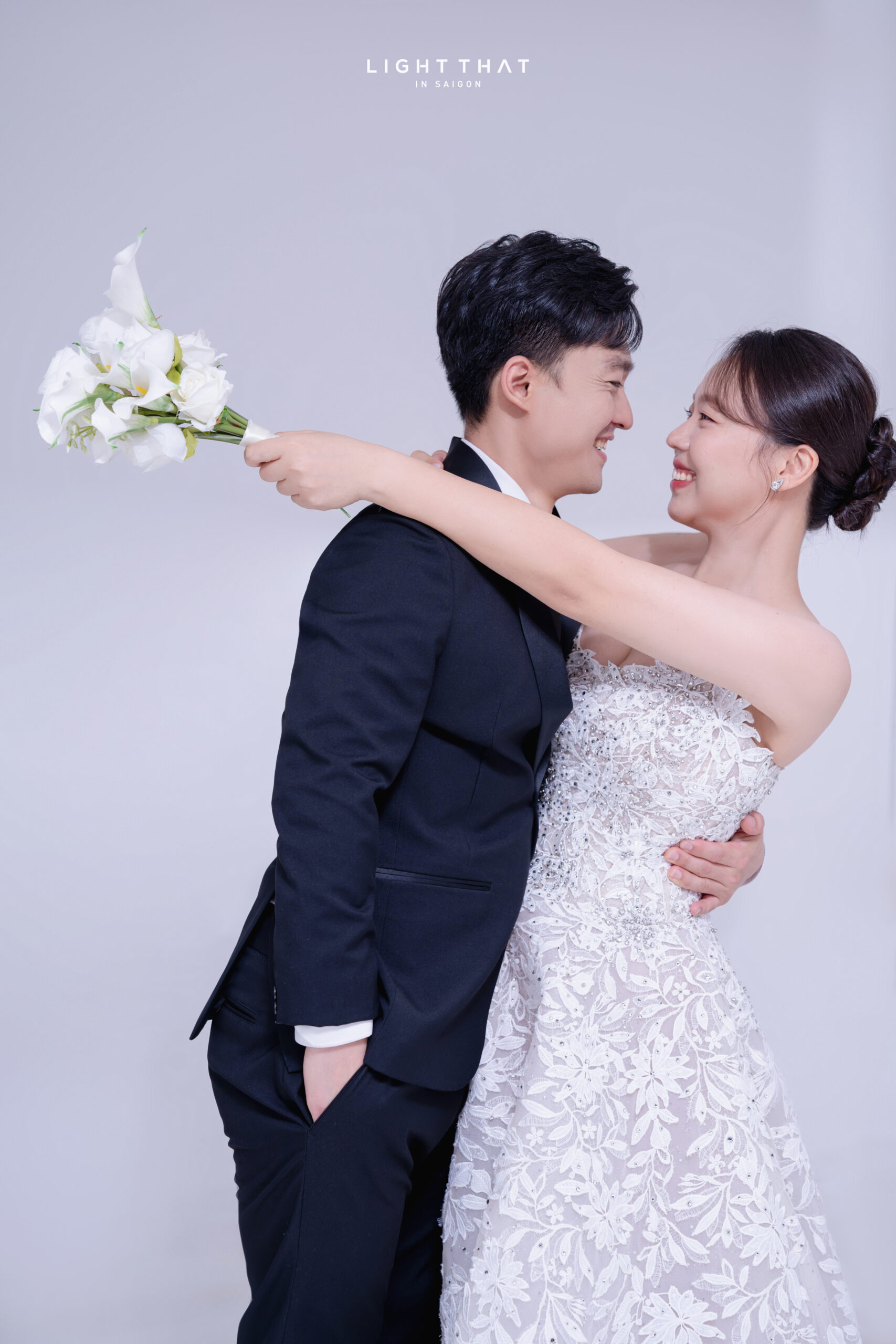 Cô dâu chú rể tạo dáng đơn giản, đứng cạnh nhau trong bộ ảnh cưới phông trơn đen sang trọng và tự nhiên