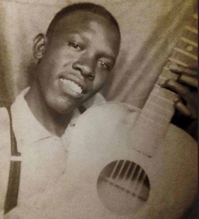Một bức ảnh cũ chụp Robert Johnson thời trẻ đang ôm chặt cây đàn guitar vào ngực.
