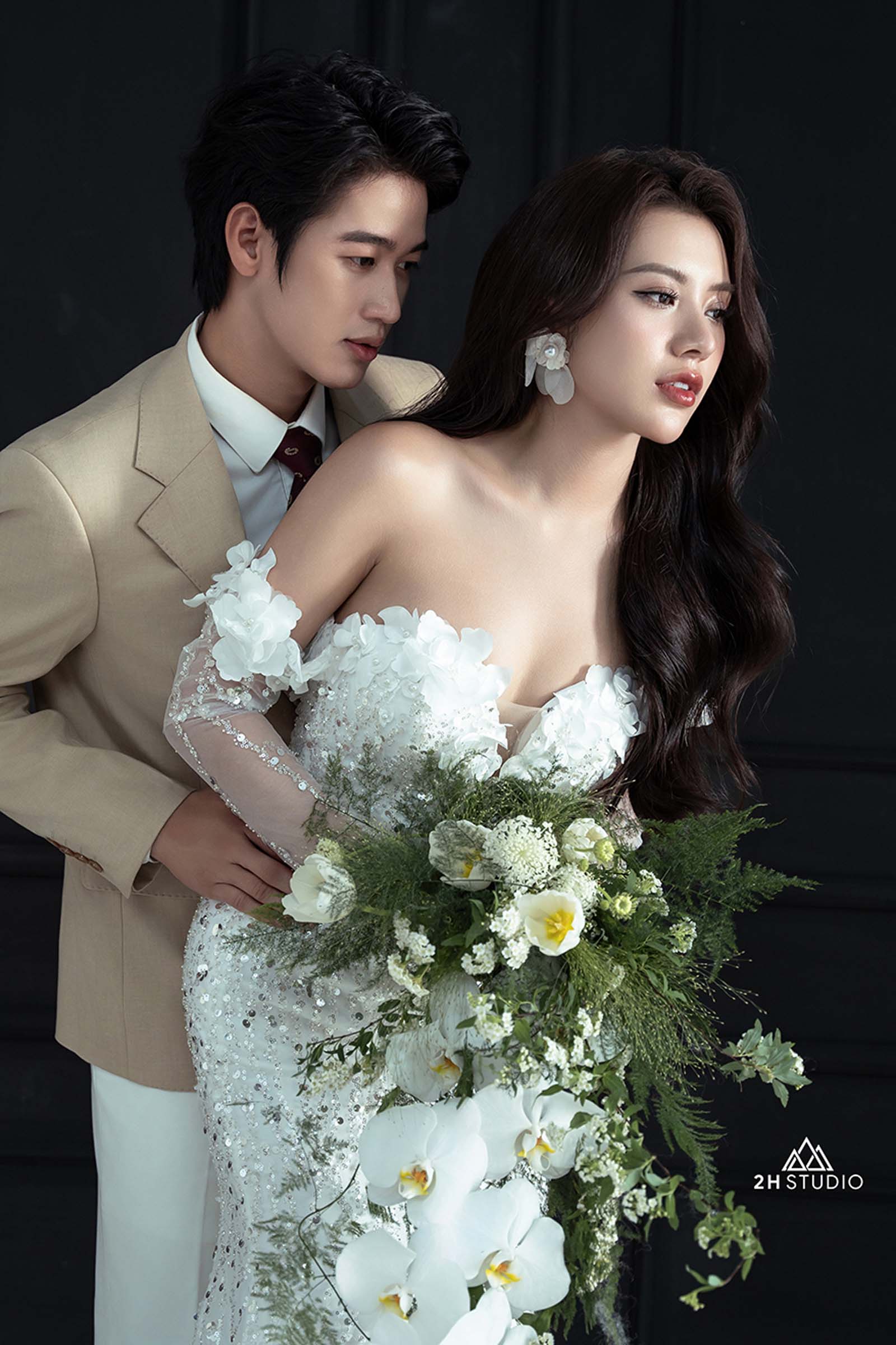 Chú rể ôm cô dâu từ phía sau ánh sáng dịu nhẹ chiếu lên