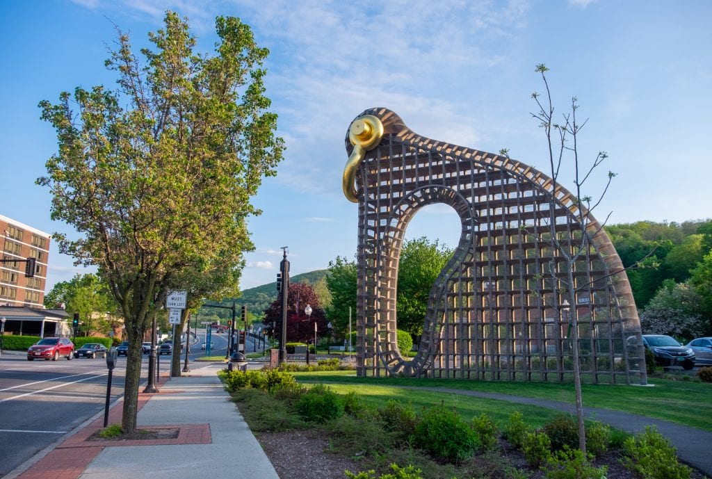 A metal gridded sculpture on the grass that looks a bit like a modern interpretation of a bird, a gold handle serving as the beak and eyeball. It