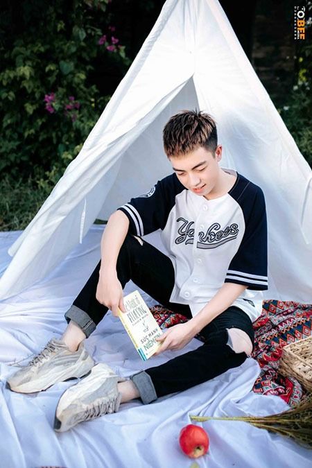 tạo dáng với tư thế ngồi như một nam sinh nho nhã cầm trên tay quyển sách